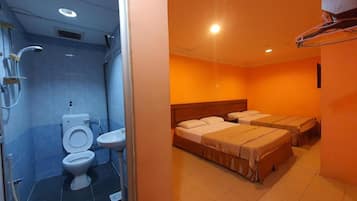 A hotel room with a bathroom containing a toilet, sink, and shower. There are two beds with headboards and a small table.