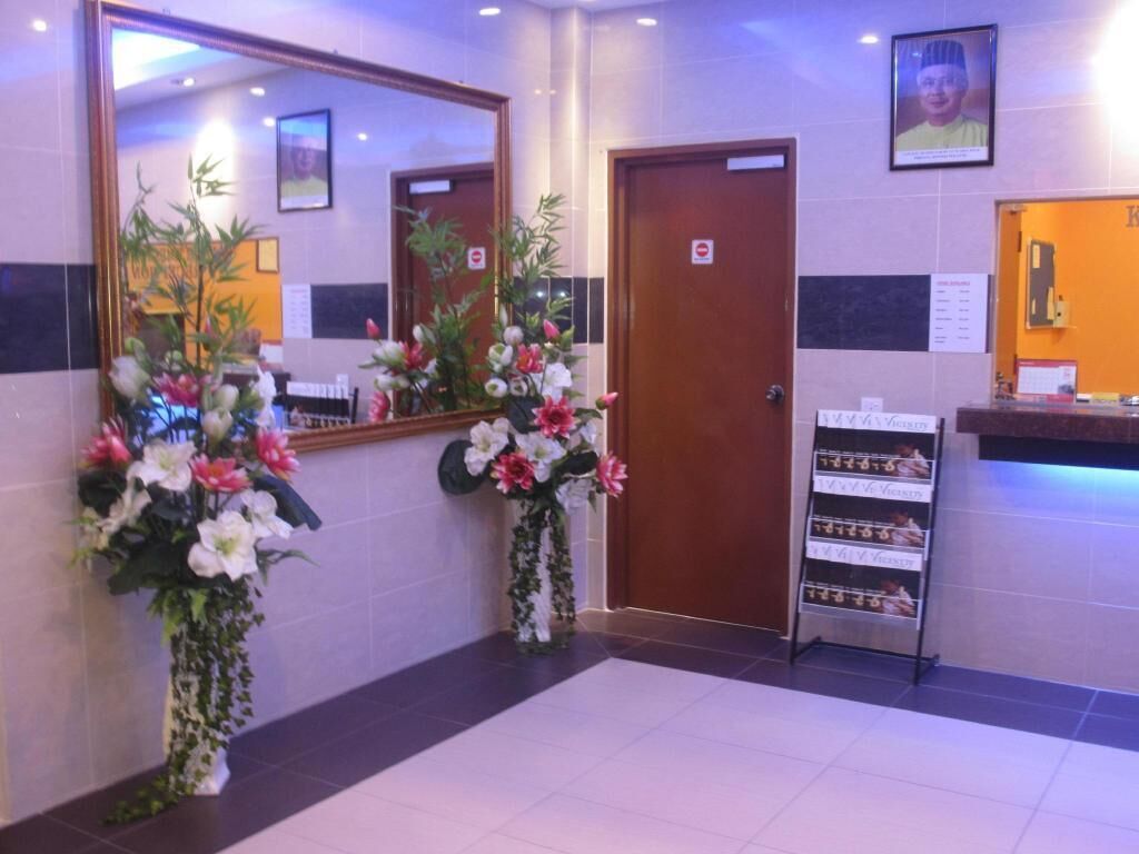 A hotel lobby with a reception desk, a large mirror, and two flower arrangements.