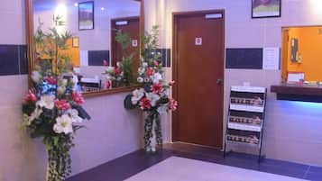 A hotel lobby with a reception desk, a large mirror, and two flower arrangements.
