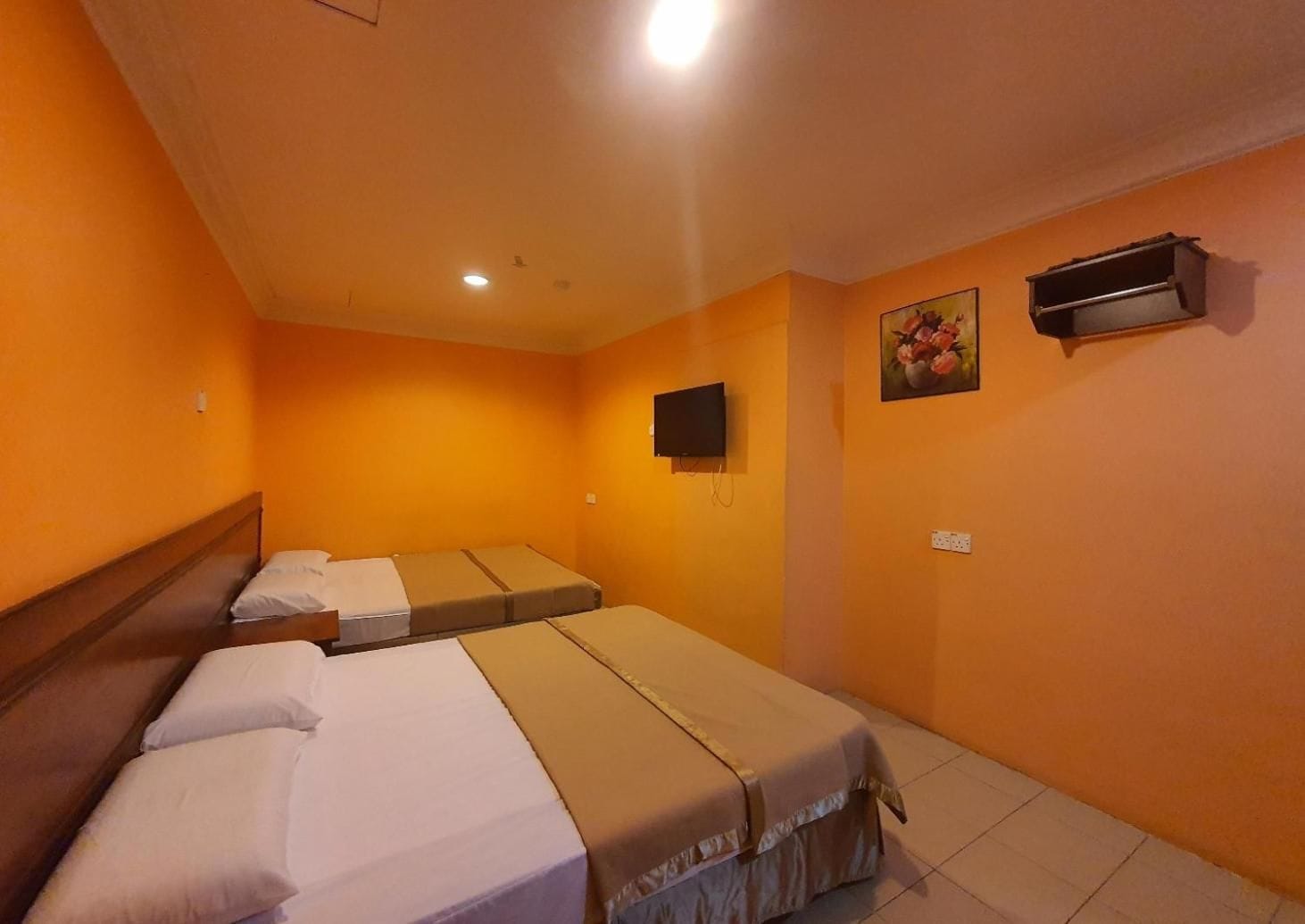 A hotel room with three single beds, a television mounted on the wall, and a small air conditioning unit.