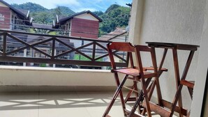Un balcón con una silla y una mesa de madera, con vista a una zona residencial con casas y una montaña al fondo.