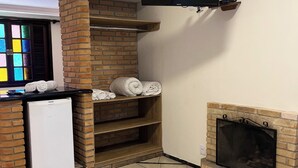 Un espacio habitable compacto con una chimenea de ladrillo, un televisor de pantalla plana montado en la pared, un refrigerador pequeño y un mueble empotrado con toallas dobladas.