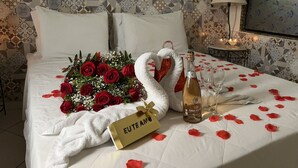 Una cama impecable con un ramo de rosas rojas, una toalla con forma de cisne, una botella de champán y una caja de regalo 'EUTE AMOR'.