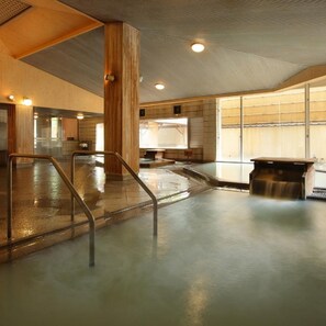 Une piscine intérieure moderne, dotée d’une paroi en verre, de colonnes en bois et d’un banc.