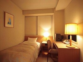 Una habitación de hotel con cama, escritorio, silla, lámpara y un cuadro en la pared.