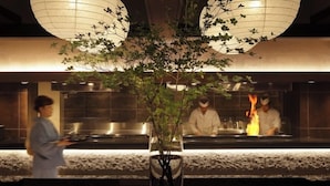 Restaurante com um vaso central de folhagem, cozinheiros ao fundo e design de interiores moderno.