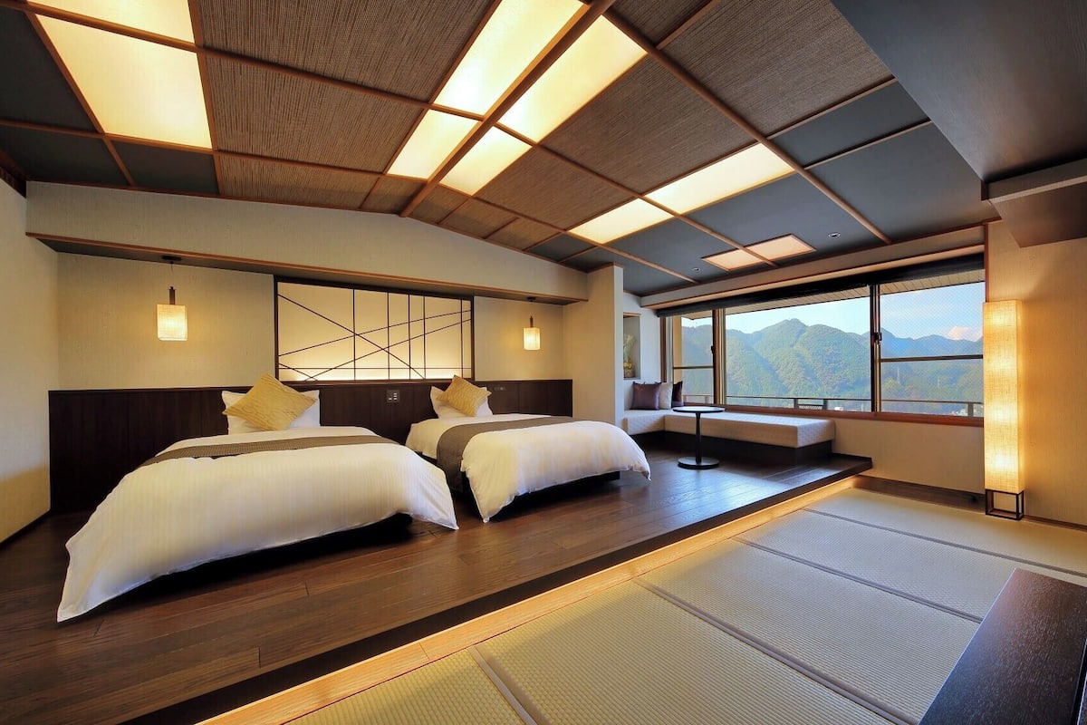 Habitación de hotel con dos camas, vistas a montañas y piso con tatami tradicional.