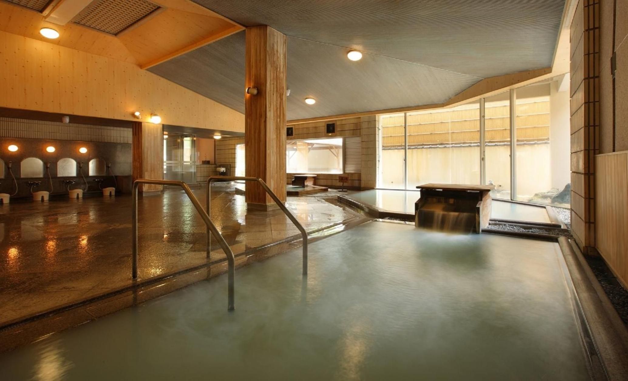Un amplio espacio interior con piscina que cuenta con varios accesos, una zona de estar central y vistas al exterior a través de grandes ventanales.