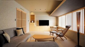 Sala de estar moderna com sofá, mesa de centro, televisão e área de estar junto a uma janela.