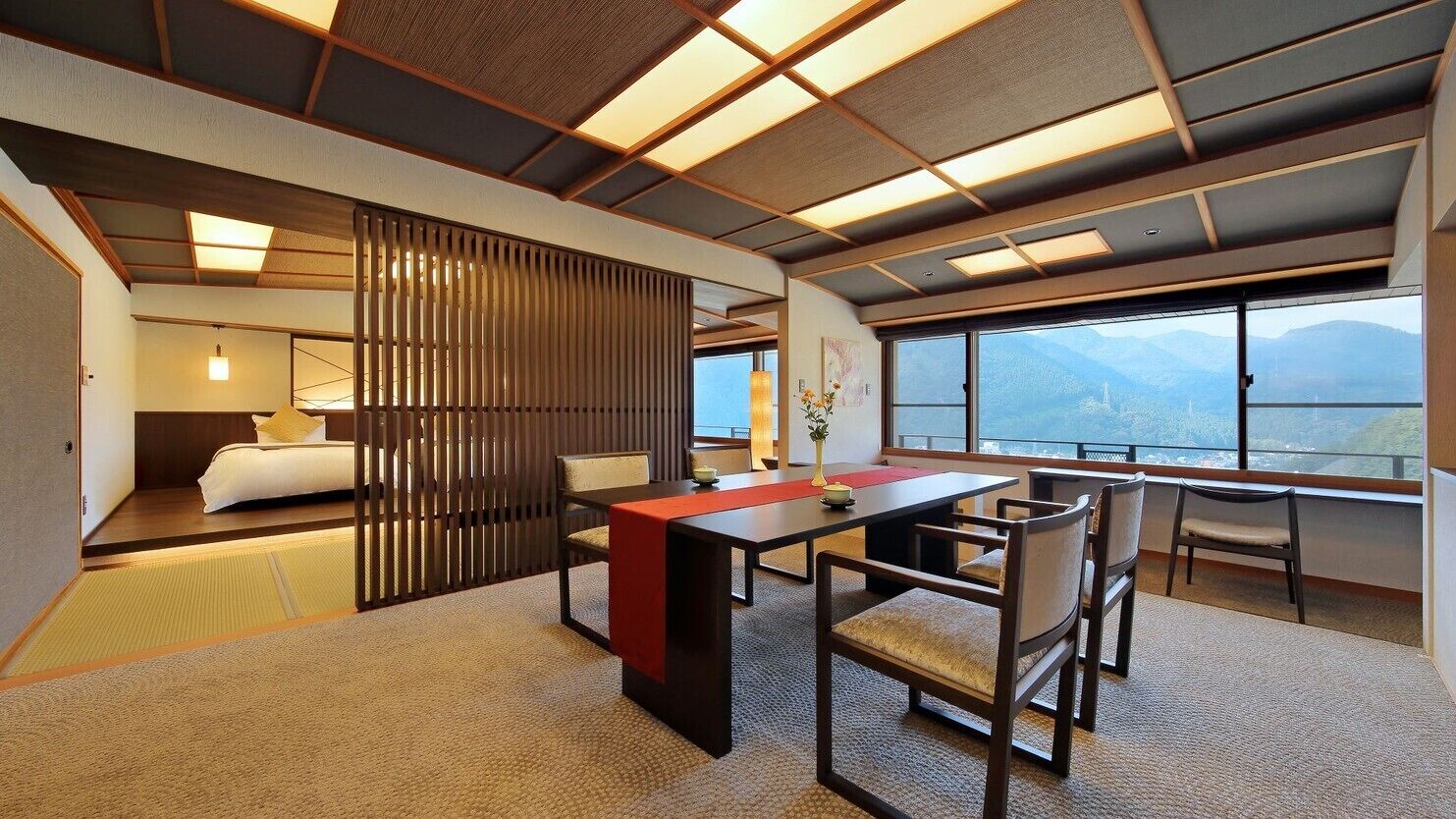 Habitación de hotel con cama, mesa de comedor, sillas y vistas a las montañas, además de una puerta corrediza.