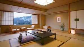 A traditional Japanese room with tatami flooring, a low table, and a view of a mountainous landscape.