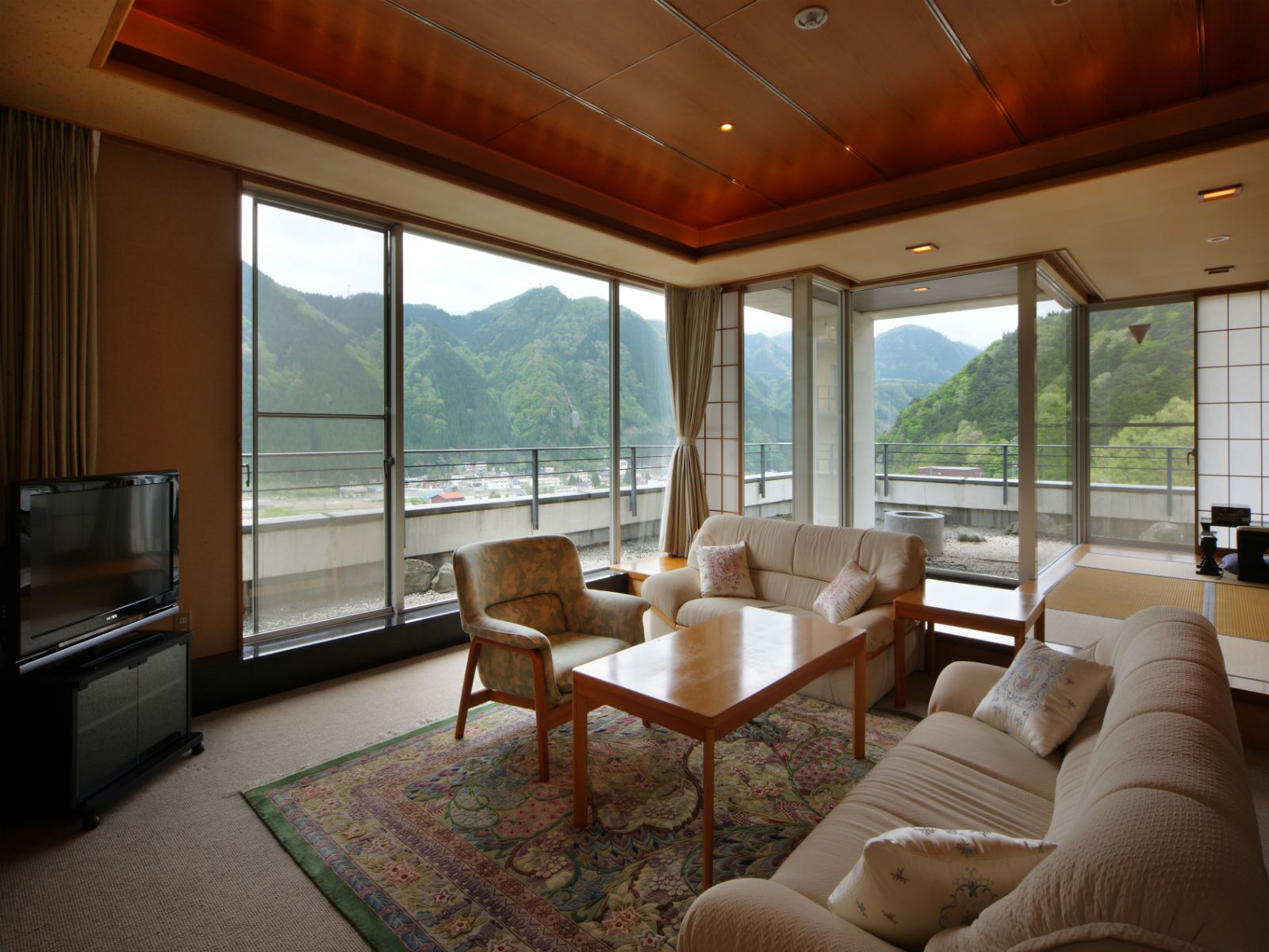 Habitación con sofá, sillas, mesa, televisión y ventanas amplias con vistas a la montaña.