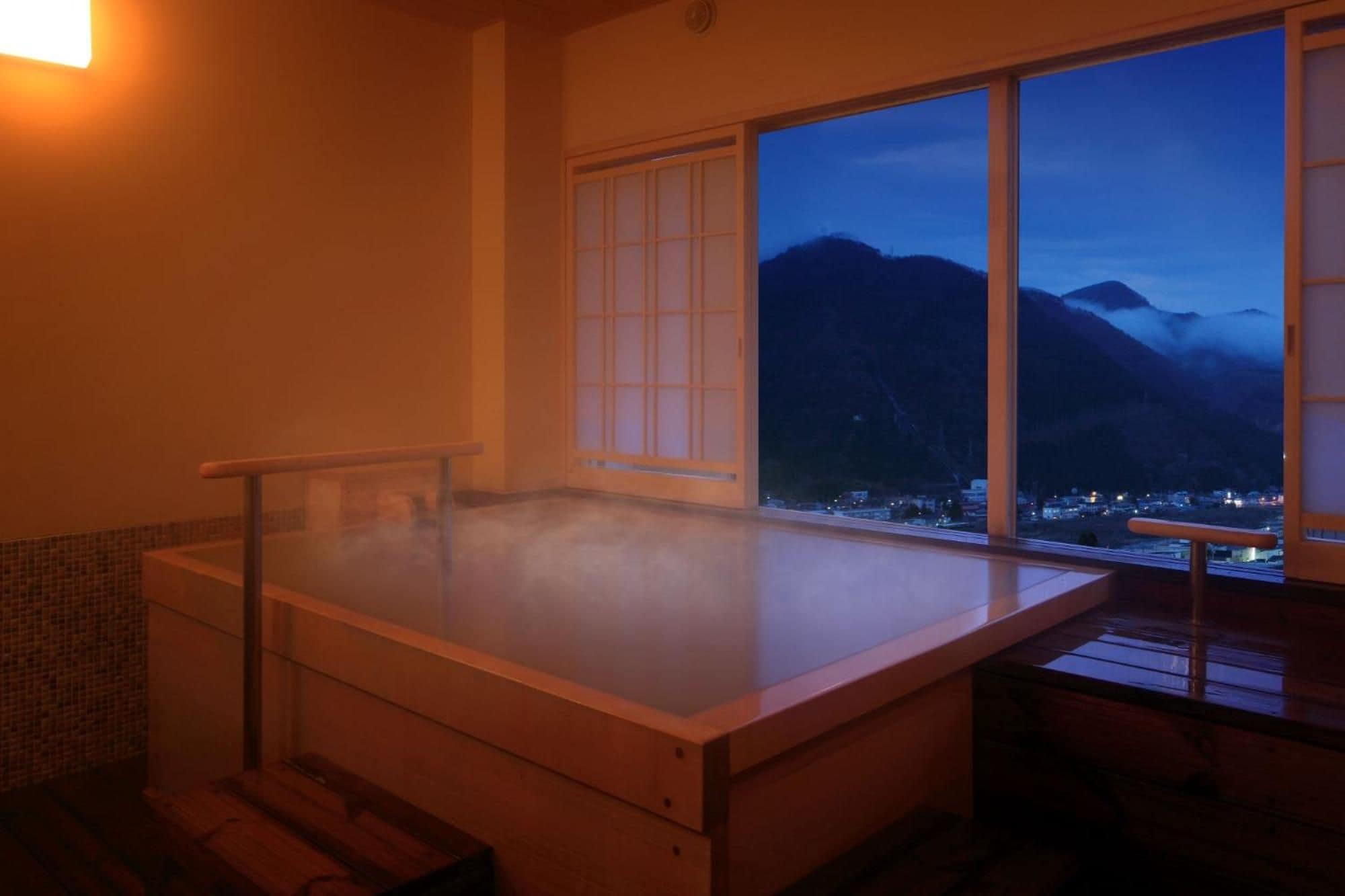 A hot spring bath with a view of mountains and a town at dusk.