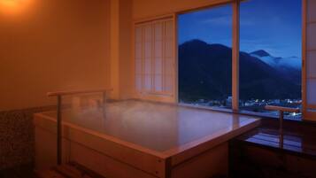 A hot spring bath with a view of mountains and a town at dusk.