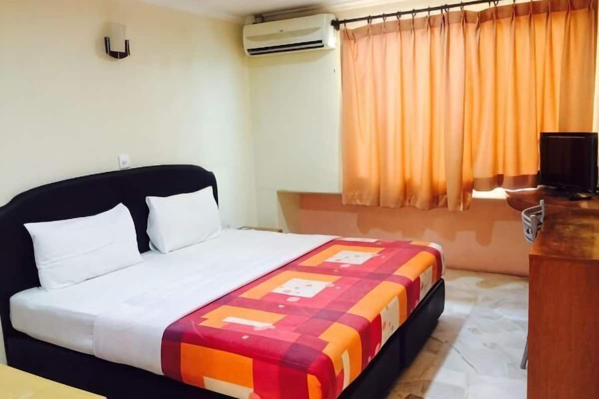 A hotel room with a bed, a desk, an air conditioner, and a window with curtains.