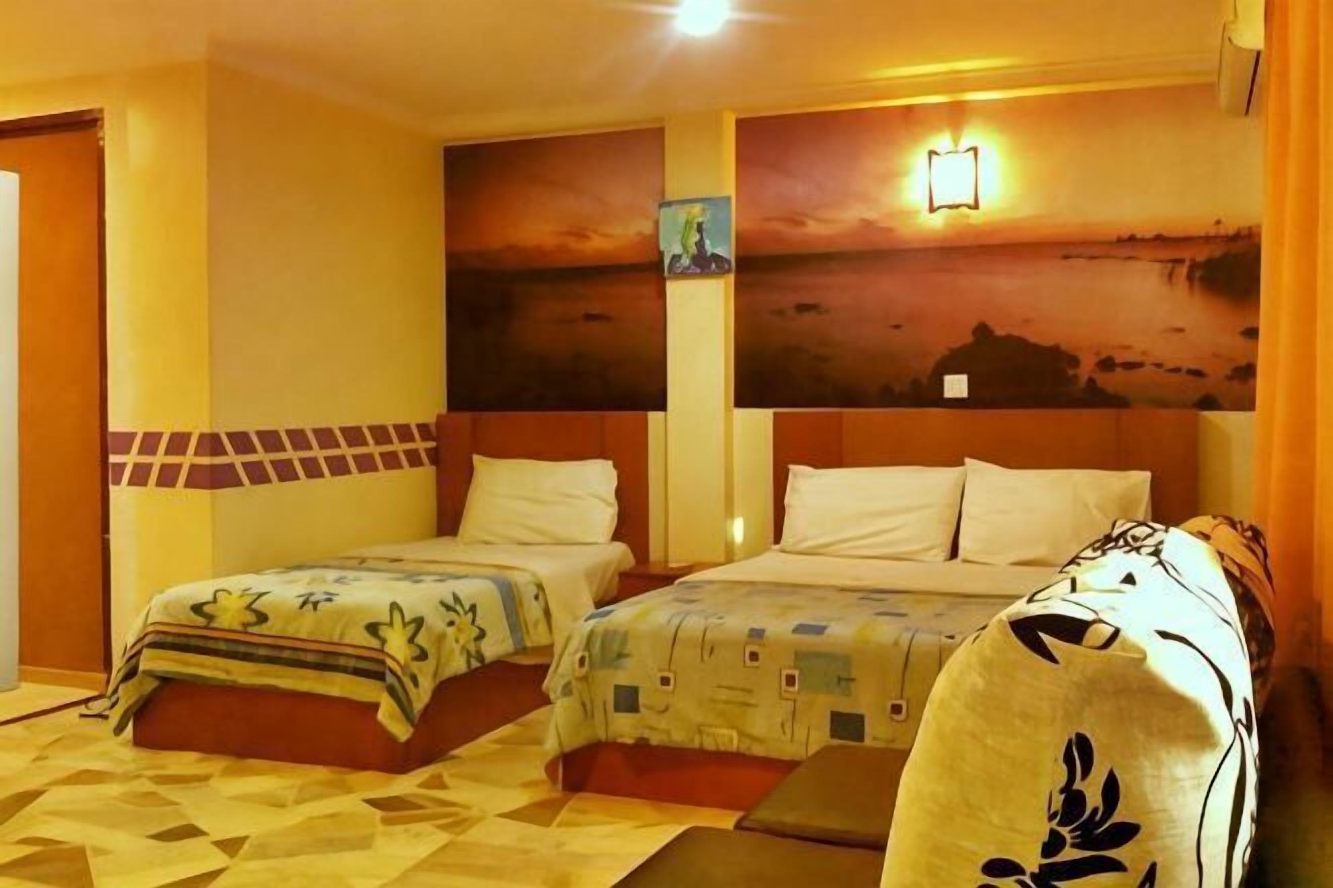 Una habitación de hotel con dos camas, un cuadro grande en la pared y una mesita de noche.