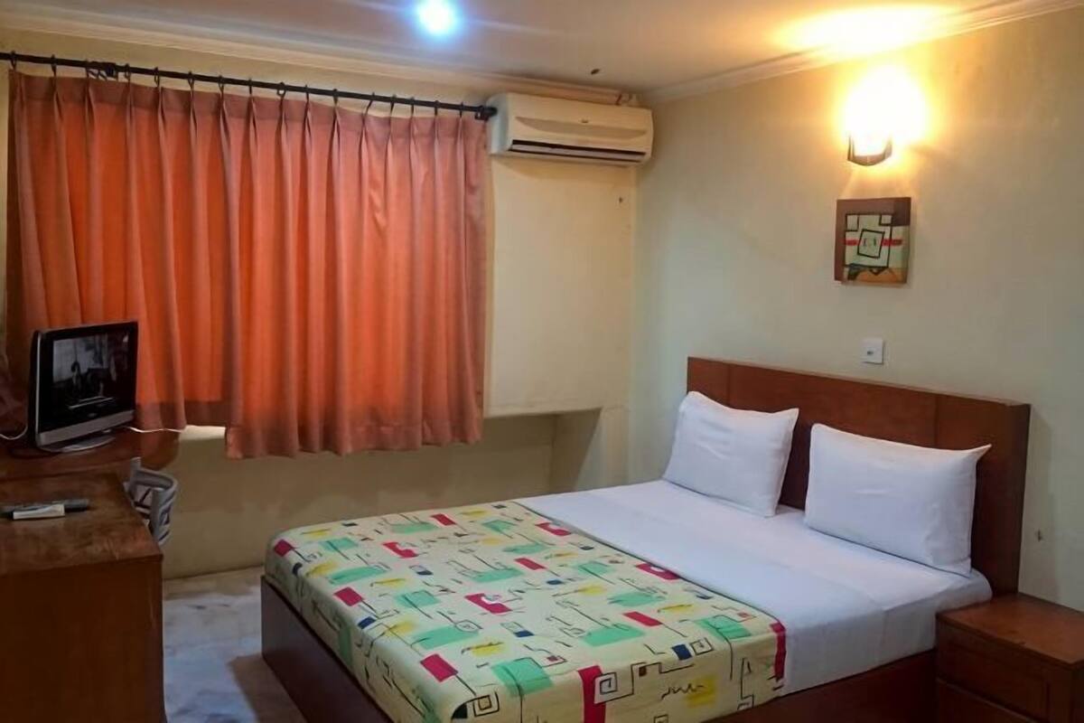 A hotel room with a bed, a desk, an air conditioner, and a wall-mounted light.
