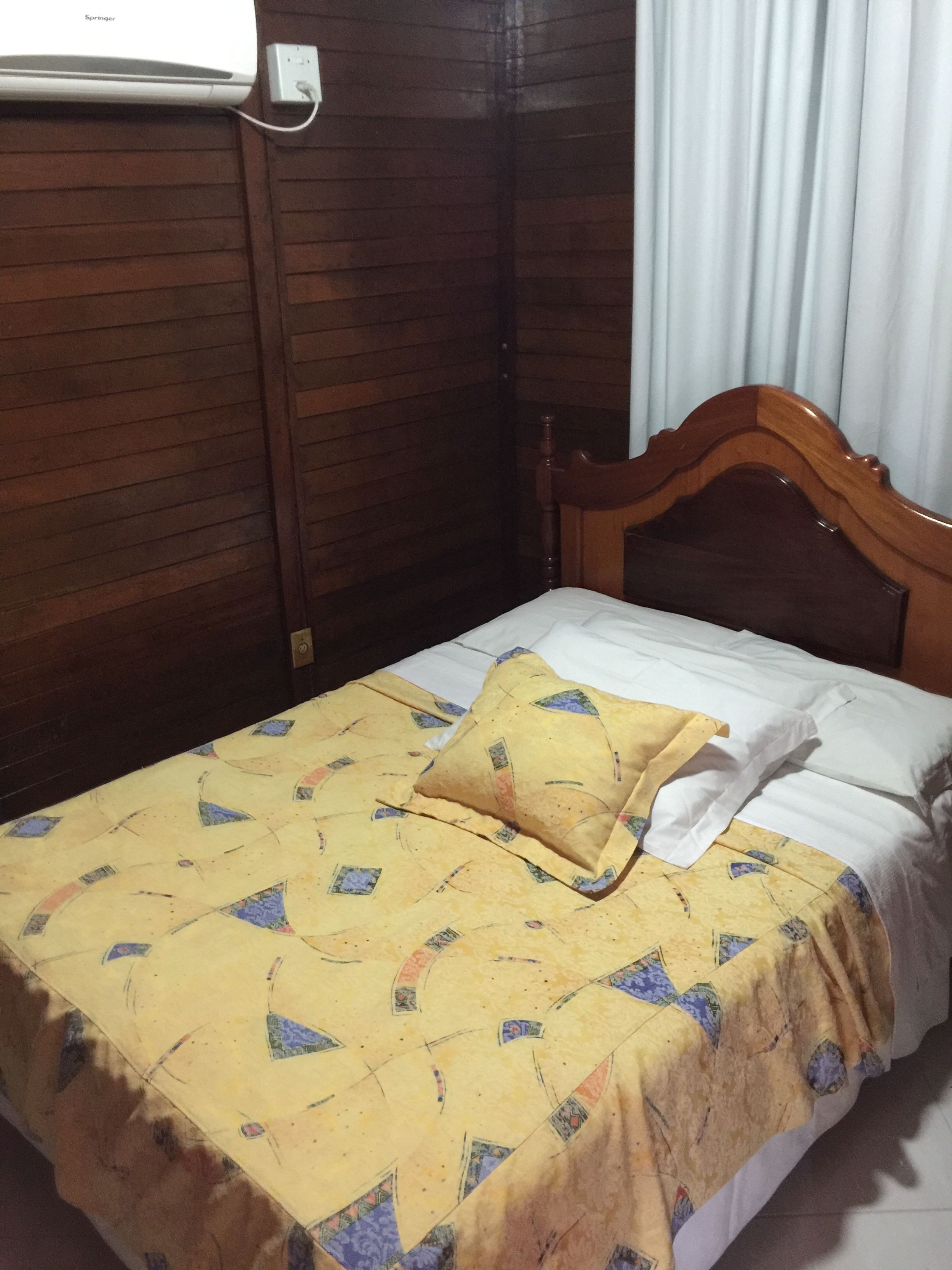 Un lit simple avec une tête de lit en bois, une couvre-lit jaune à motifs et un oreiller blanc.