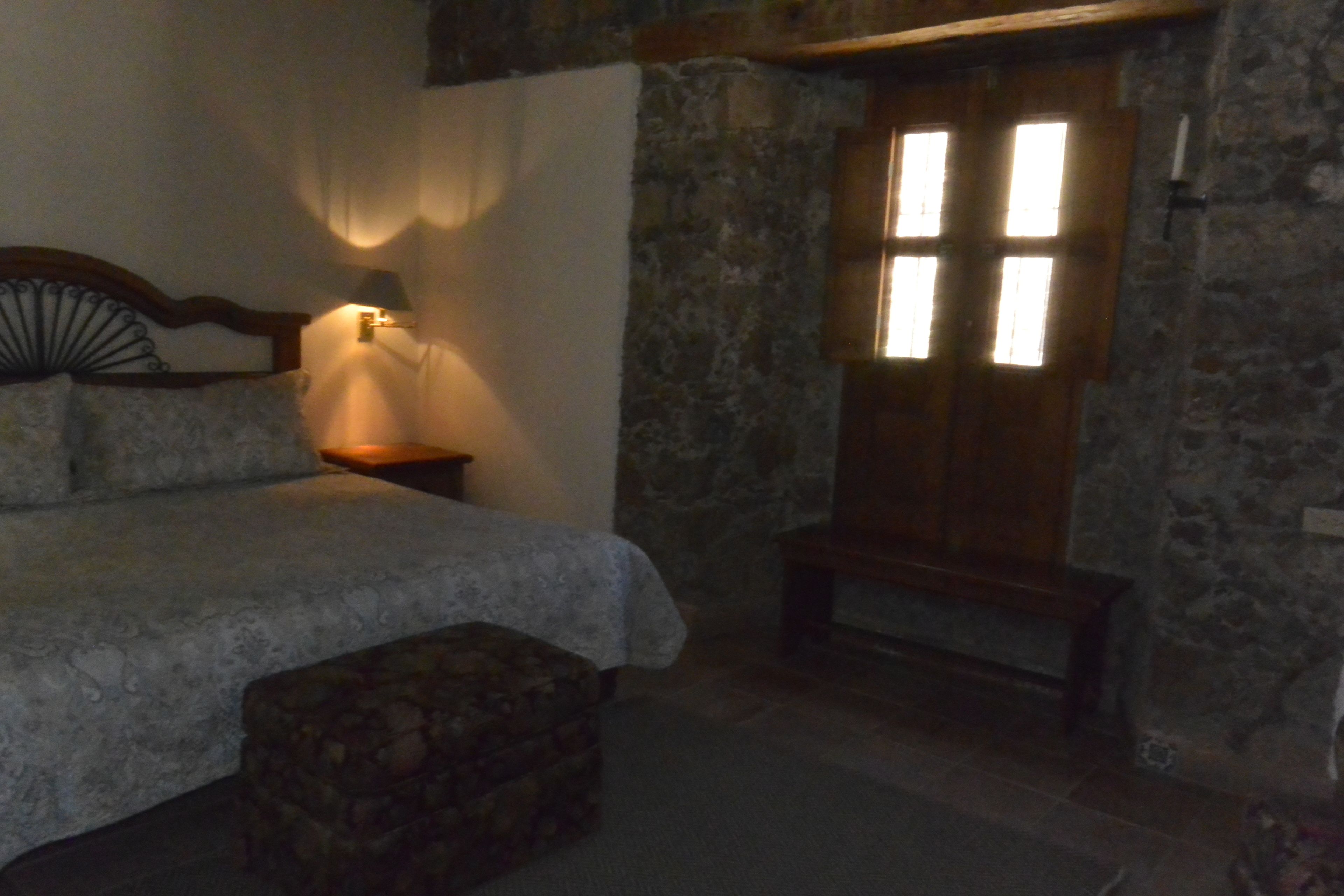 A bedroom with a stone wall, a wooden bed, a nightstand, and a bench.