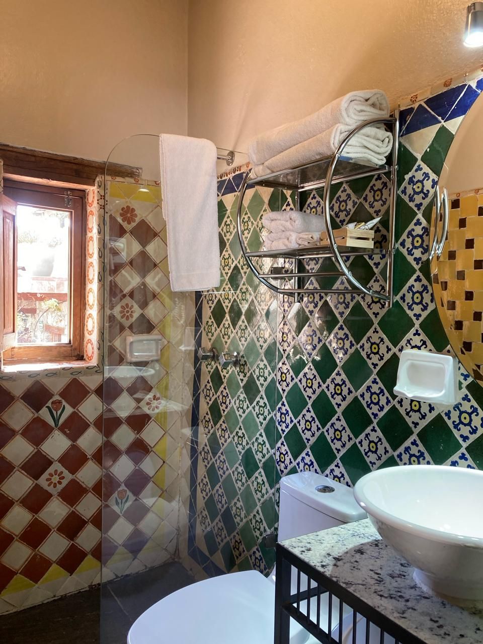 Un baño con pared de azulejos, una ventana, un lavamanos y un perchero para toallas.