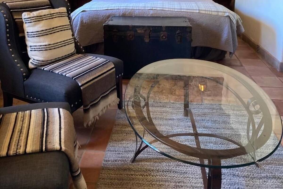 Een gezellige slaapkamer met een stenen muur, een houten plafond, een bed met witte lakens, een gestreept fauteuil, een glazen salontafel en twee bedlampen.