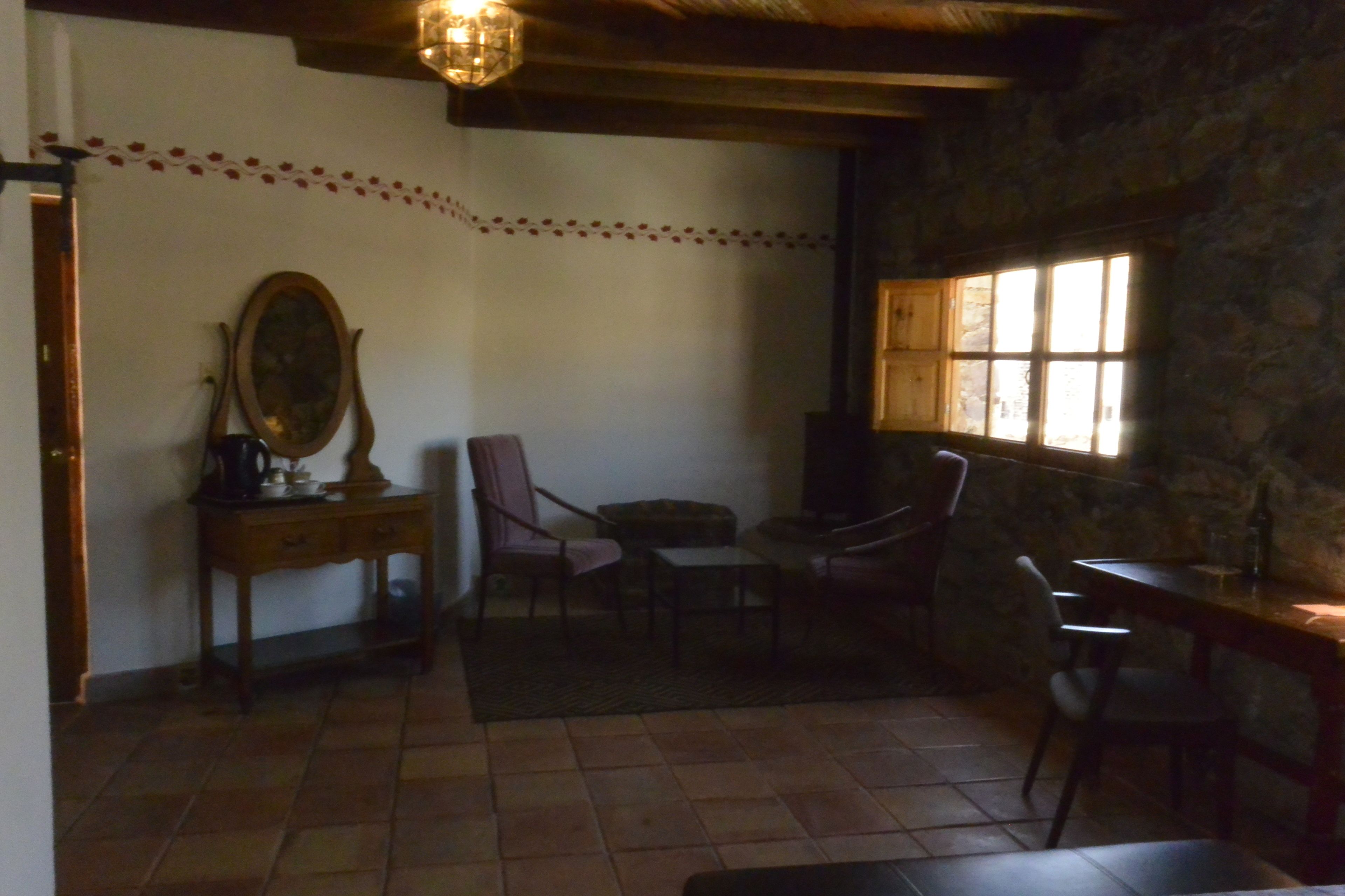 A room with a stone wall, a wooden table, a chair, a small table, and a mirror on a wooden cabinet.