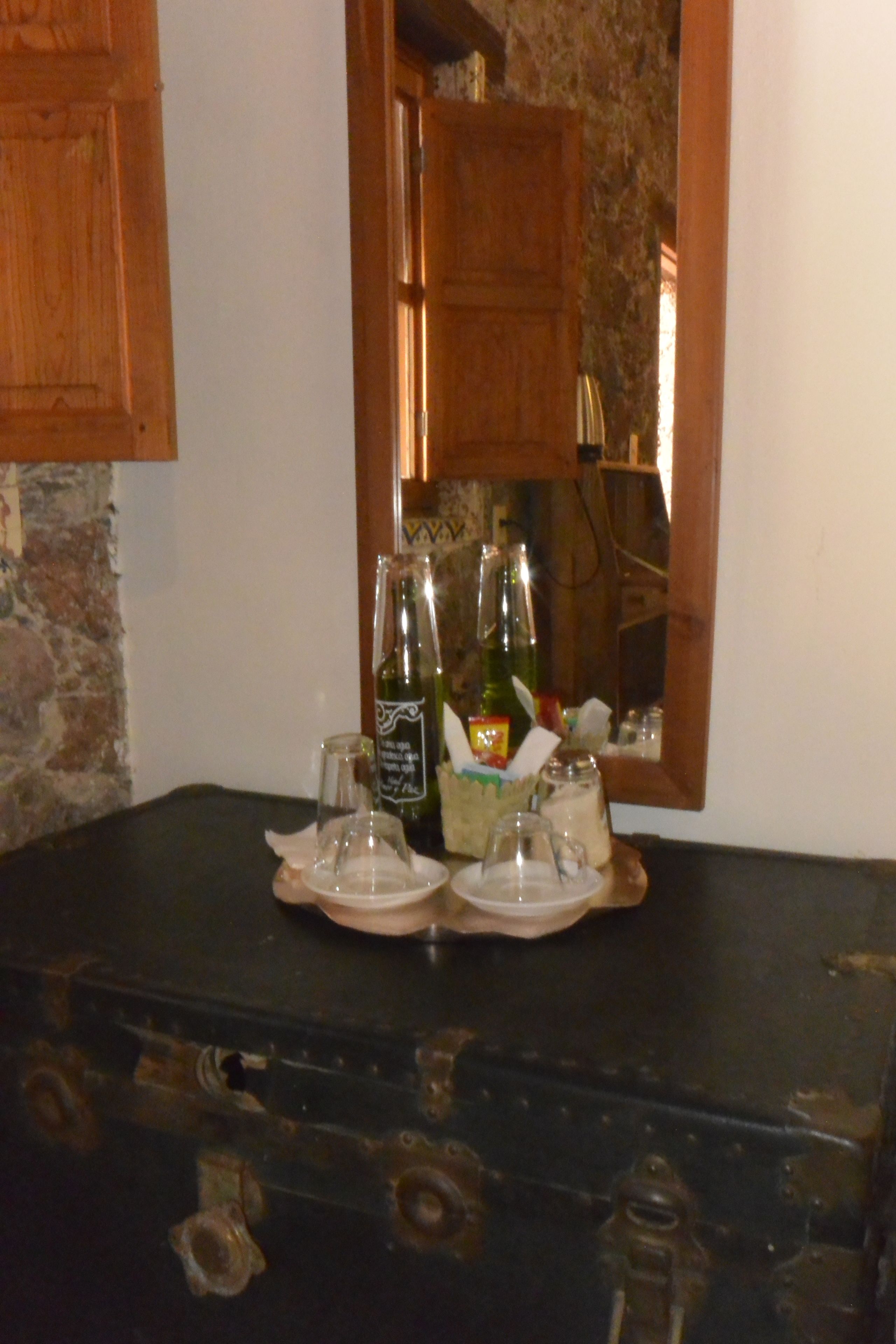 Ein Holzkabinent mit einem Spiegel, der einen Raum reflektiert. Ein Tisch im Vordergrund zeigt eine Flasche, ein Glas und einen kleinen Behälter.