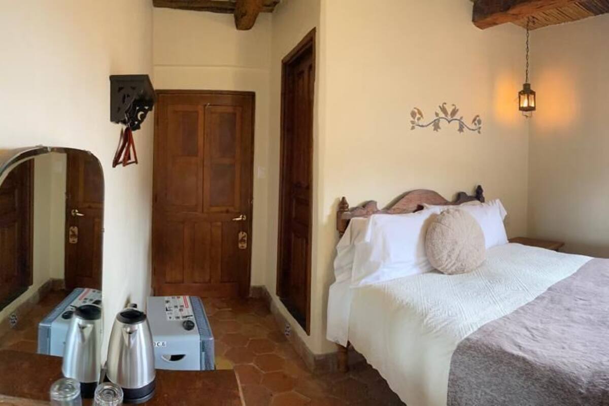 Een slaapkamer met een bed, een houten garderobe, een klein tafeltje en een spiegel.
