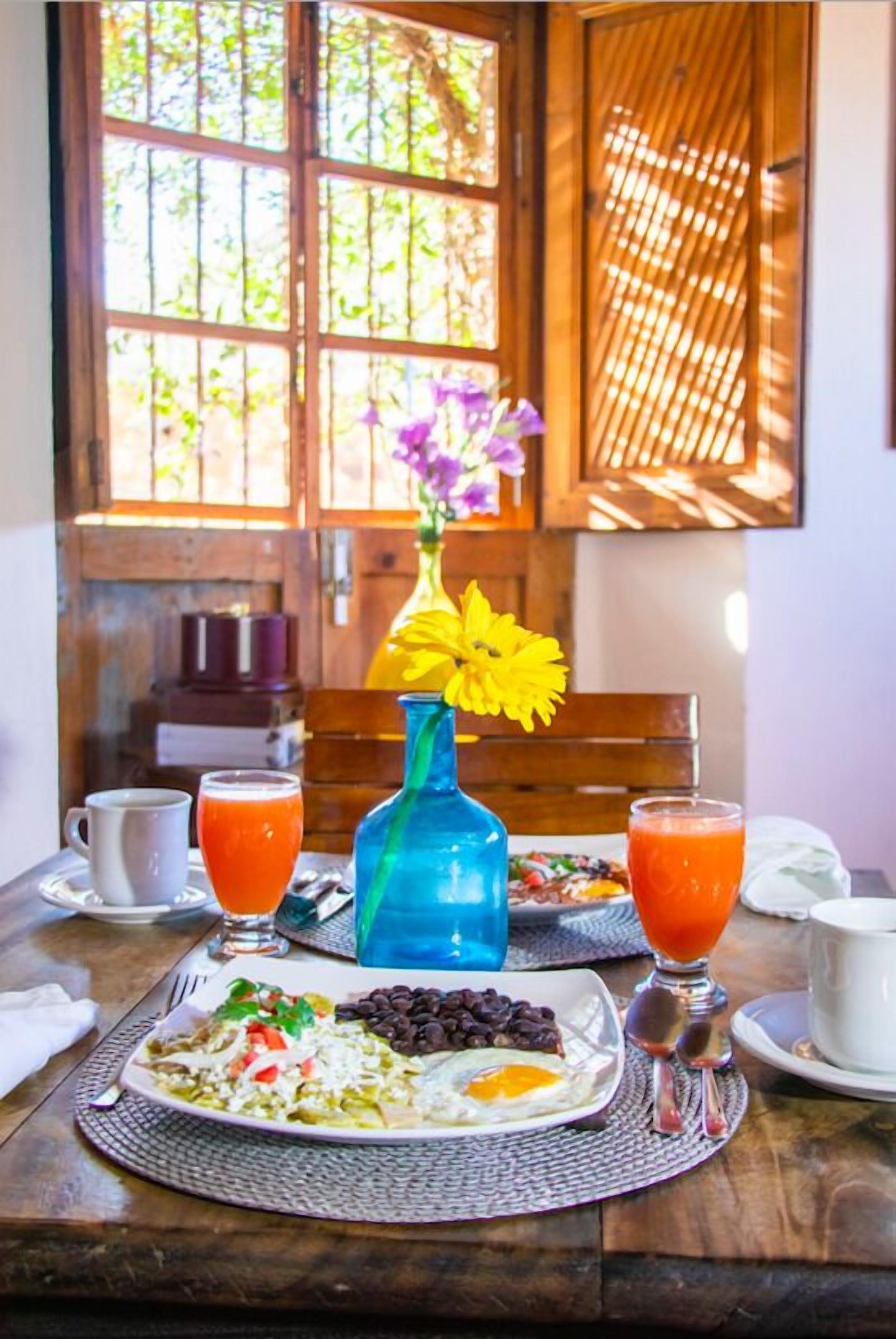 A breakfast table with a plate of food, two glasses of orange juice, and a blue vase with flowers.