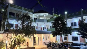 A multi-story building with a central atrium, outdoor seating area, and parked vehicles. - 99 Inn Hotel (Pak Chong)