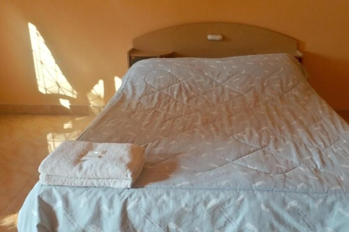 A single bed with a quilted bedspread and a folded white towel on the side.