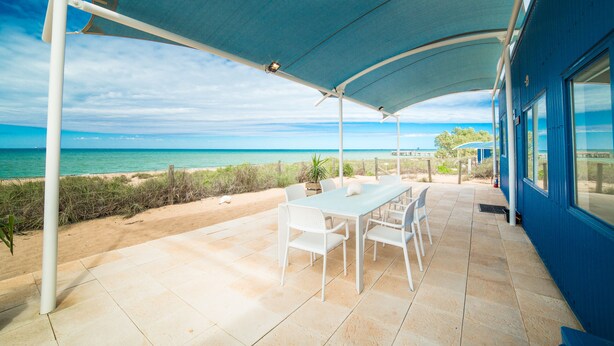 Une terrasse extérieure avec une table et des chaises, une vue sur la plage et un bâtiment bleu.