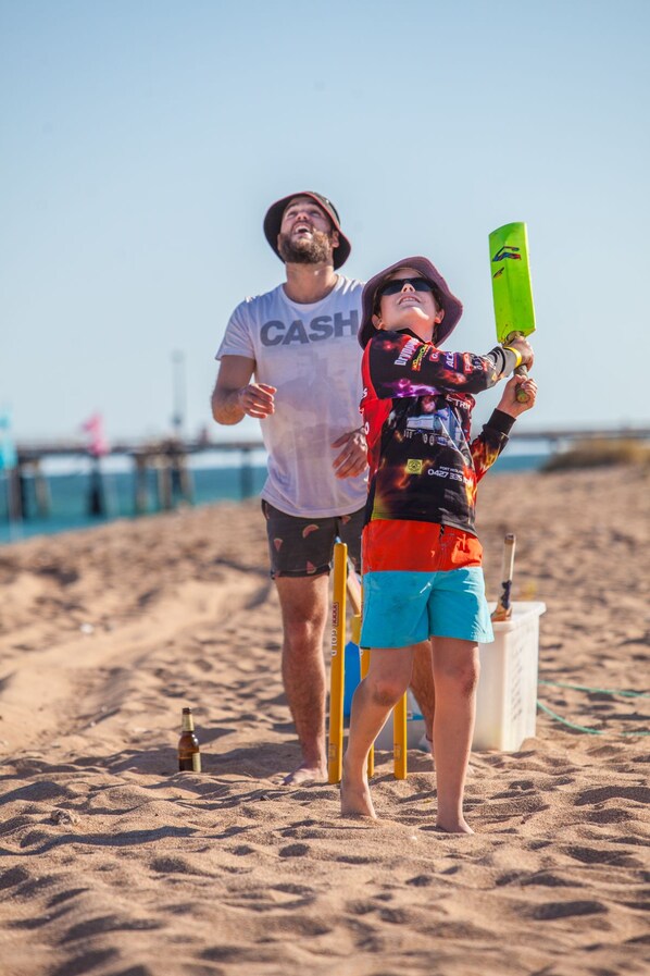 A person in a white t-shirt and shorts standing on a sandy beach, holding a cricket bat. - Mackerel Islands (Thevenard Island)