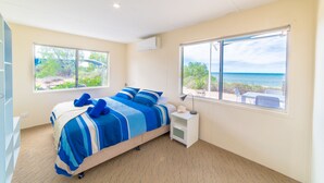 Une chambre à coucher avec un lit, deux fenêtres, une table de chevet et une vue sur la plage.