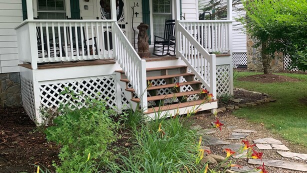 Een wit huis met veranda, trap en tuin met bloemen en planten.