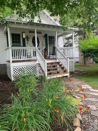 A white house with a porch, steps, and a garden with flowers and plants.