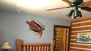 Una cama de madera con colcha escocesa, una mesita de noche de madera con una lámpara, un cabecero de madera y un ventilador de techo.