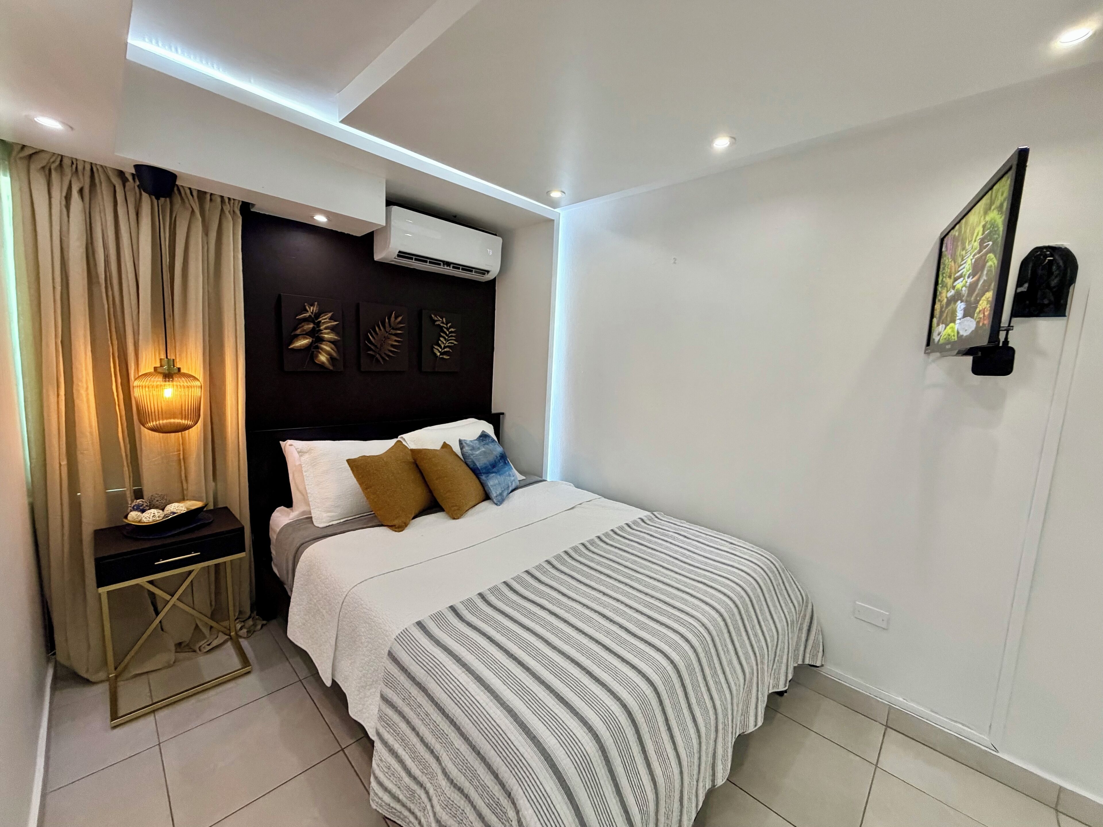 Een moderne slaapkamer met een bed, nachtkastje, airconditioning en decoratieve wandkunst.