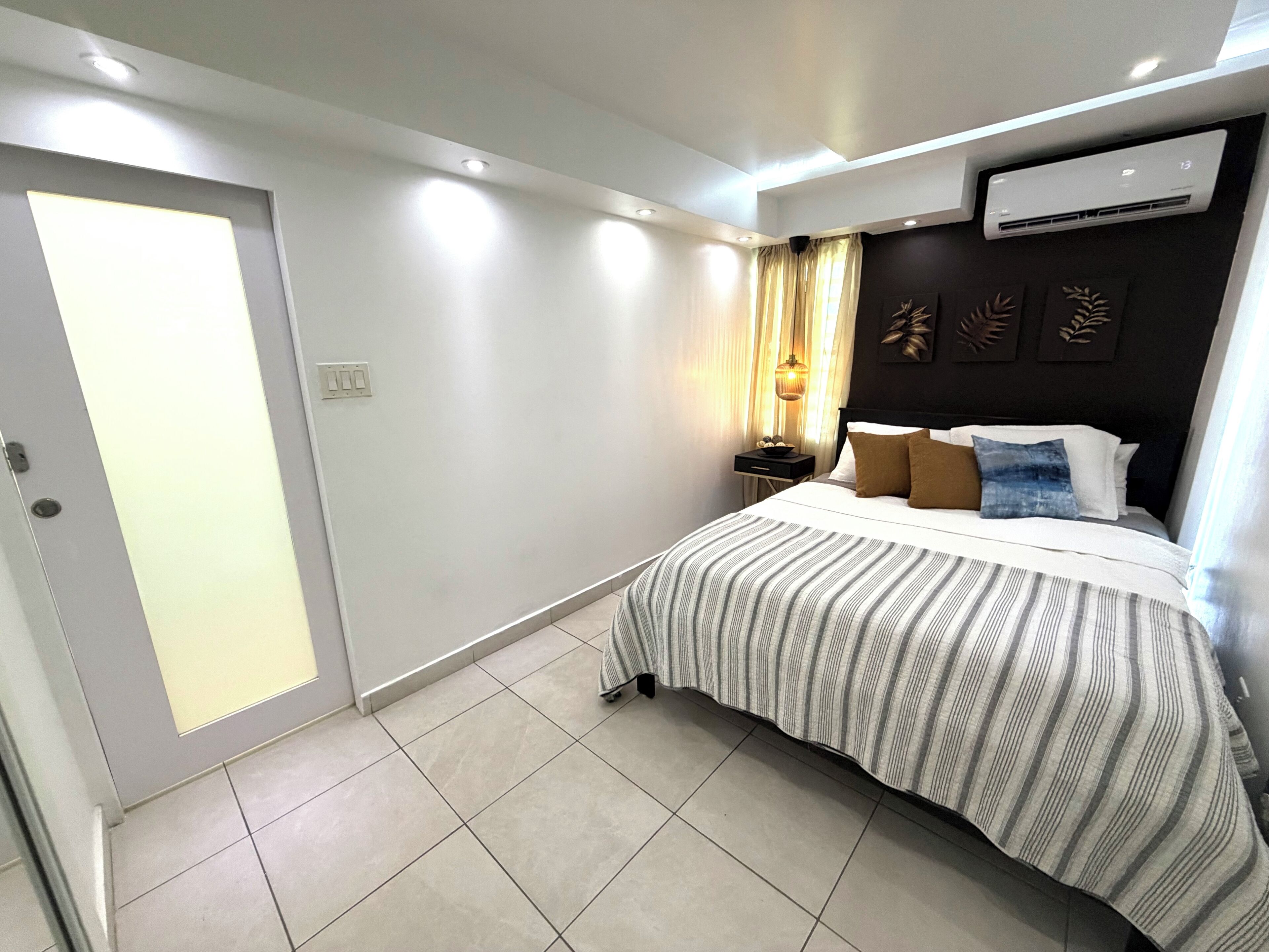Een moderne slaapkamer met een bed, nachtkastjes, een airconditioning en een schuifdeur.