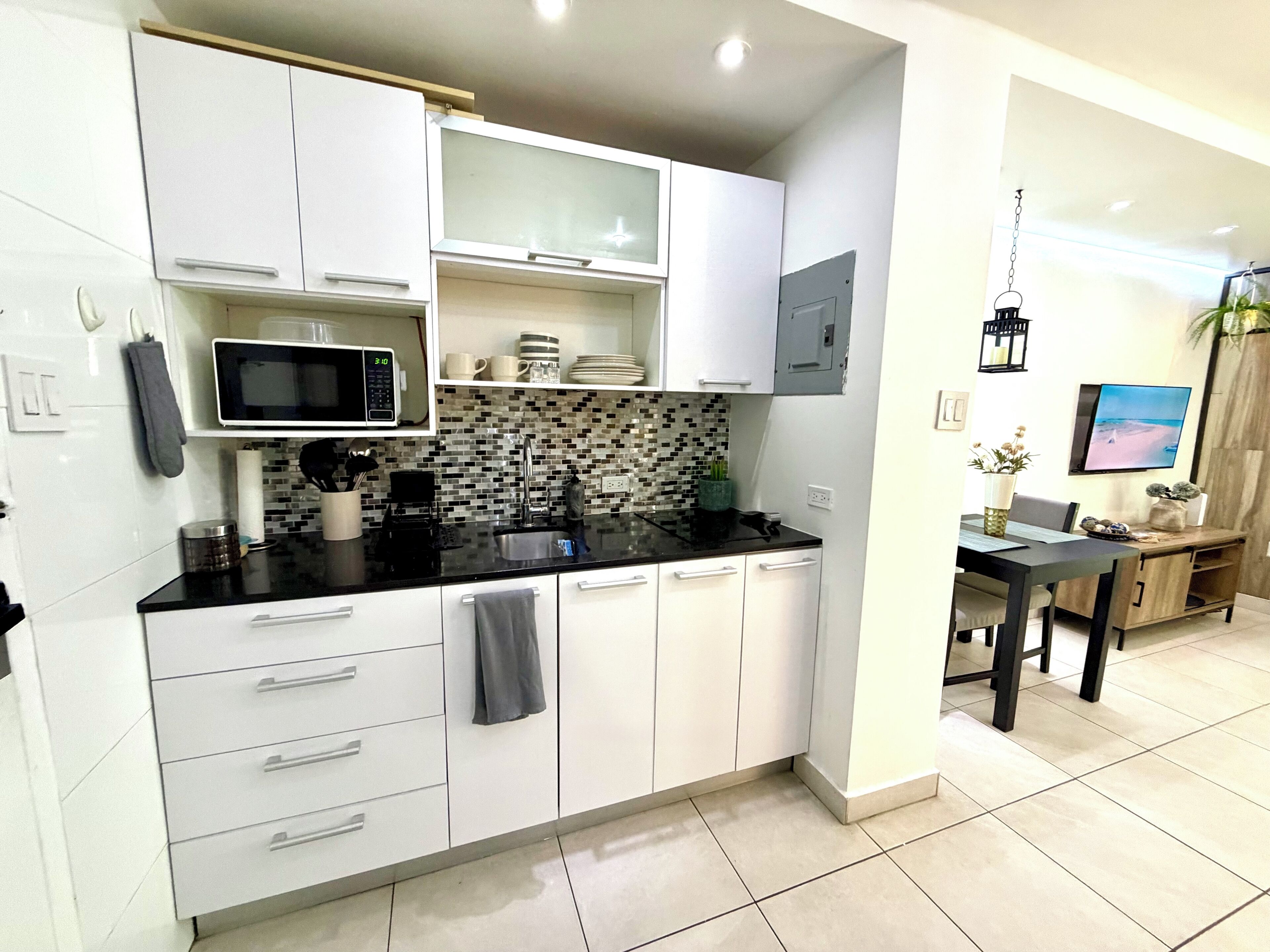 A modern kitchen with white cabinets, a black countertop, and a tiled backsplash.