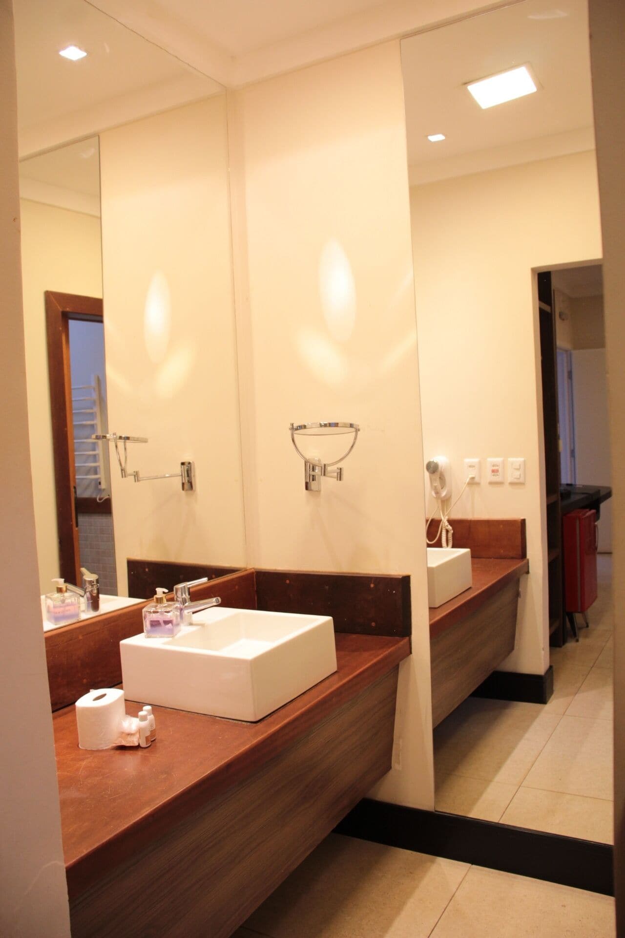 A modern bathroom with a large mirror, two sinks, and a hairdryer.