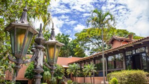 Une cour agrémentée de lampadaires décoratifs, un jardin bien entretenu et un bâtiment doté de grandes fenêtres et d’un toit recouvert de tuiles.