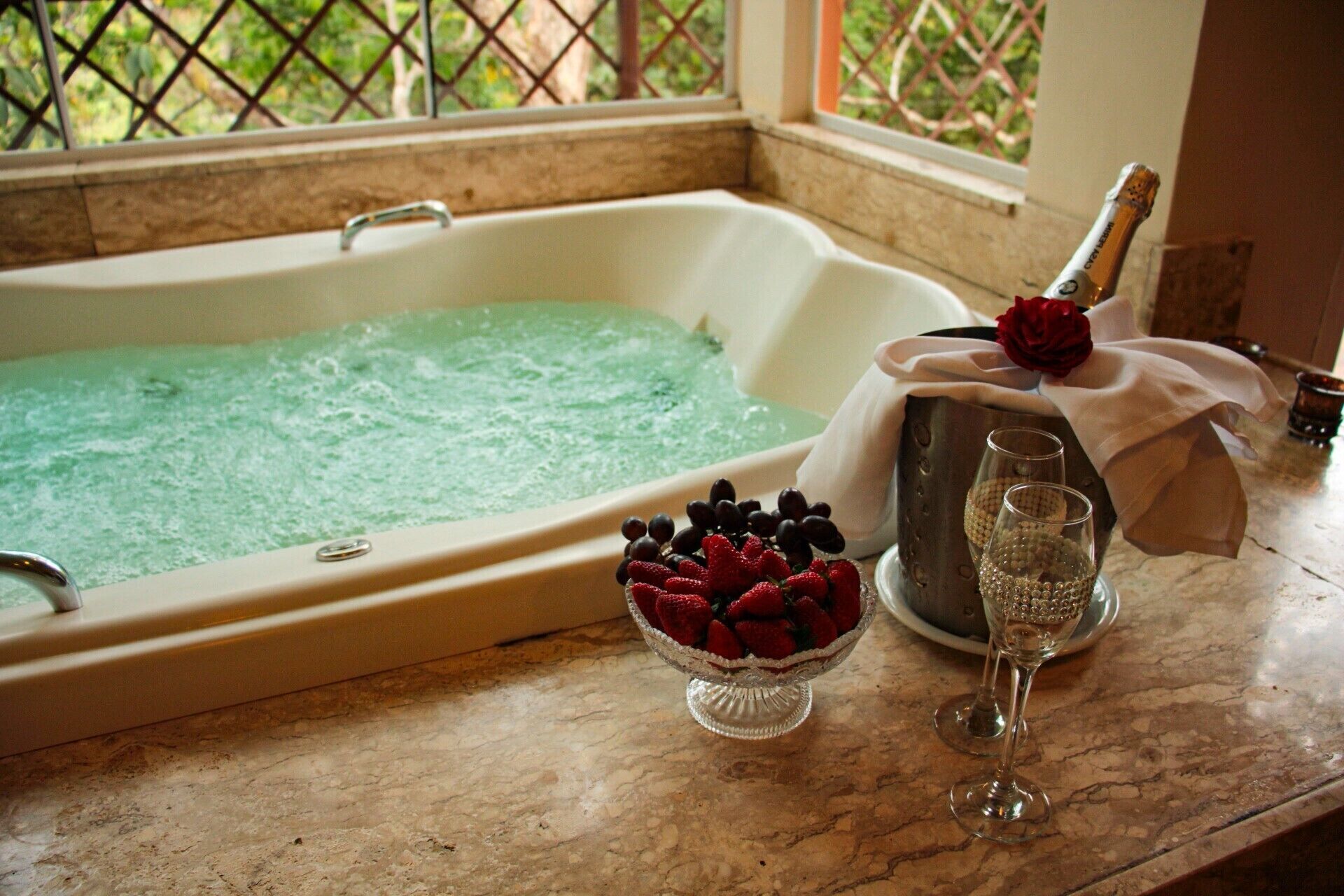 Un baño con bañera, un cuenco de fresas, una botella de champán y una copa de champán.