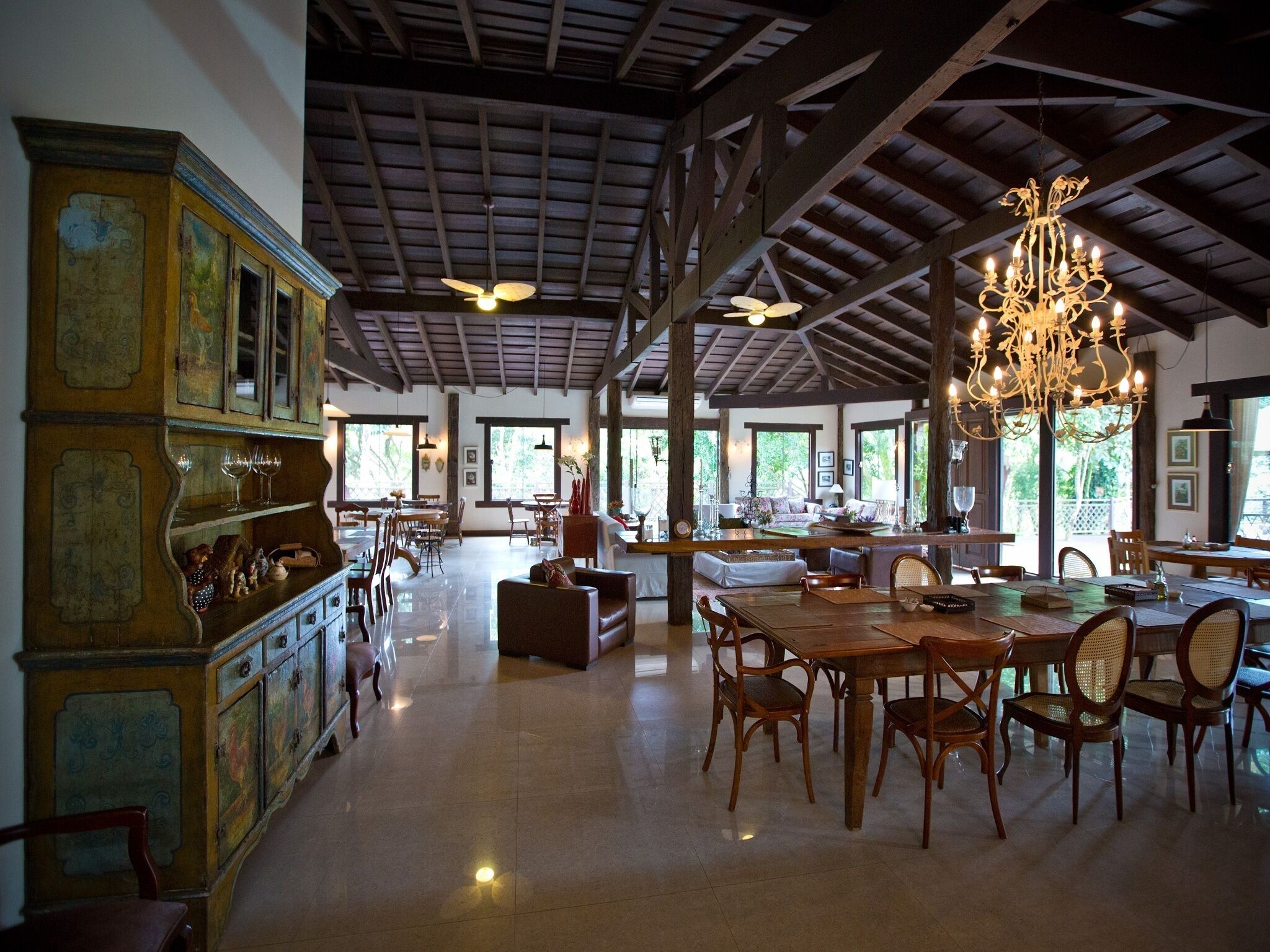 A spacious dining area with wooden furniture, a chandelier, and large windows allowing natural light.