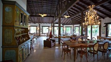 A spacious dining area with wooden furniture, a chandelier, and large windows allowing natural light.