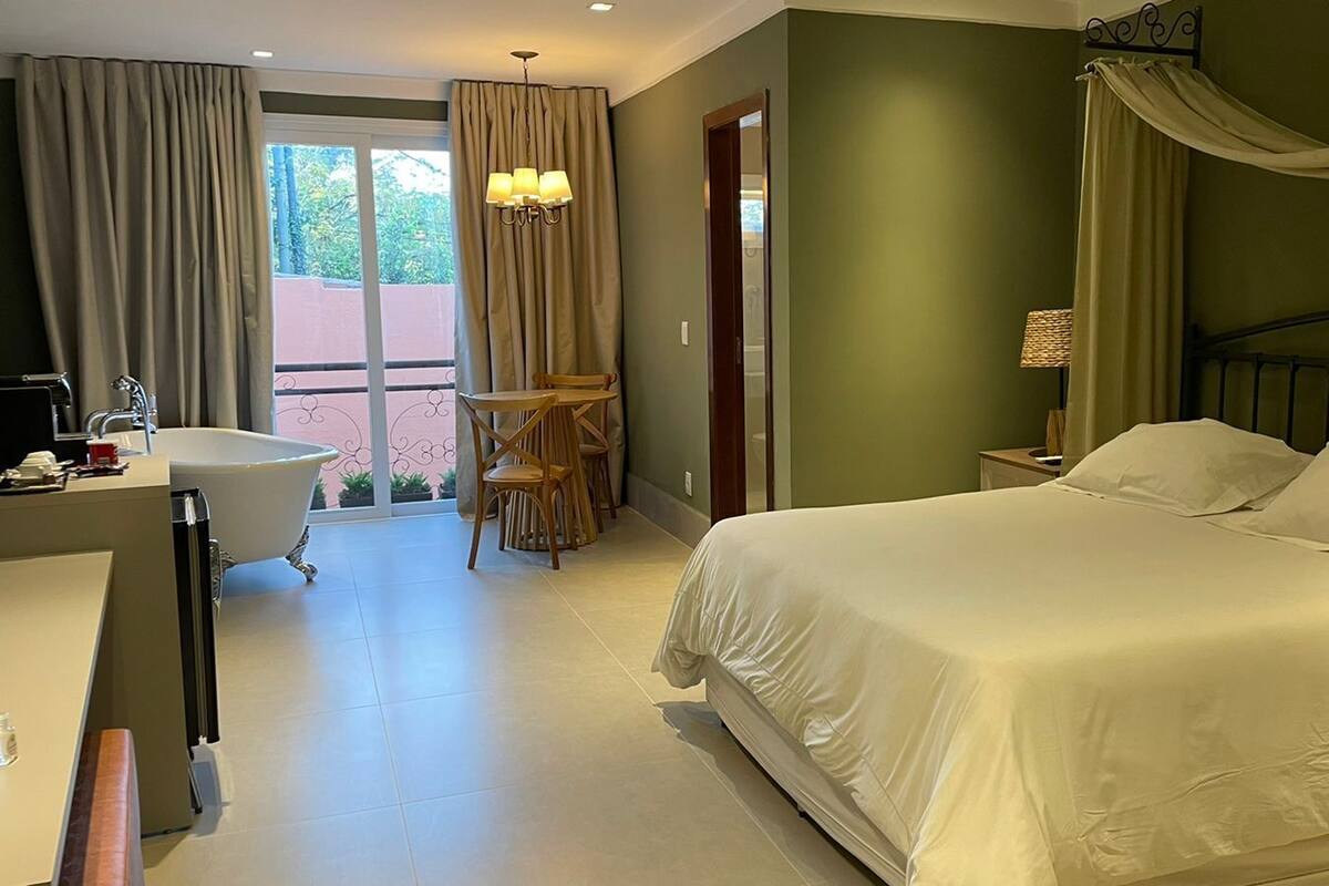 A bedroom with a large bed, a vanity with a bathtub, and a balcony with a table and chairs.