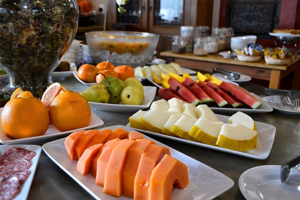 Una mesa de buffet con diversas frutas y verduras, como naranjas, manzanas y sandía.