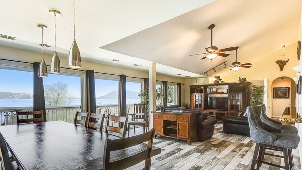 A spacious living area with a large dining table, multiple chairs, a kitchen area, and a view of the outdoors.