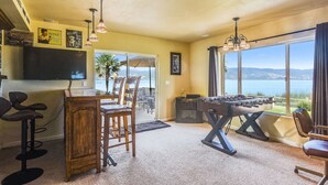 A room with a foosball table, bar area, and large windows offering a view of the outdoors.