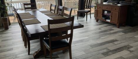 A dining area with a large wooden table and chairs, a kitchen area with a wooden cabinet, and a view of a lake through large windows.